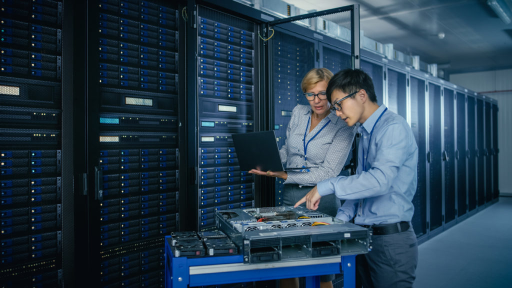 In the Modern Data Center: Engineer and IT Specialist Work with Server Racks, on a Pushcart Equipment for Installing New Hardware. Specialists Doing Maintenance and Diagnostics of the Database.